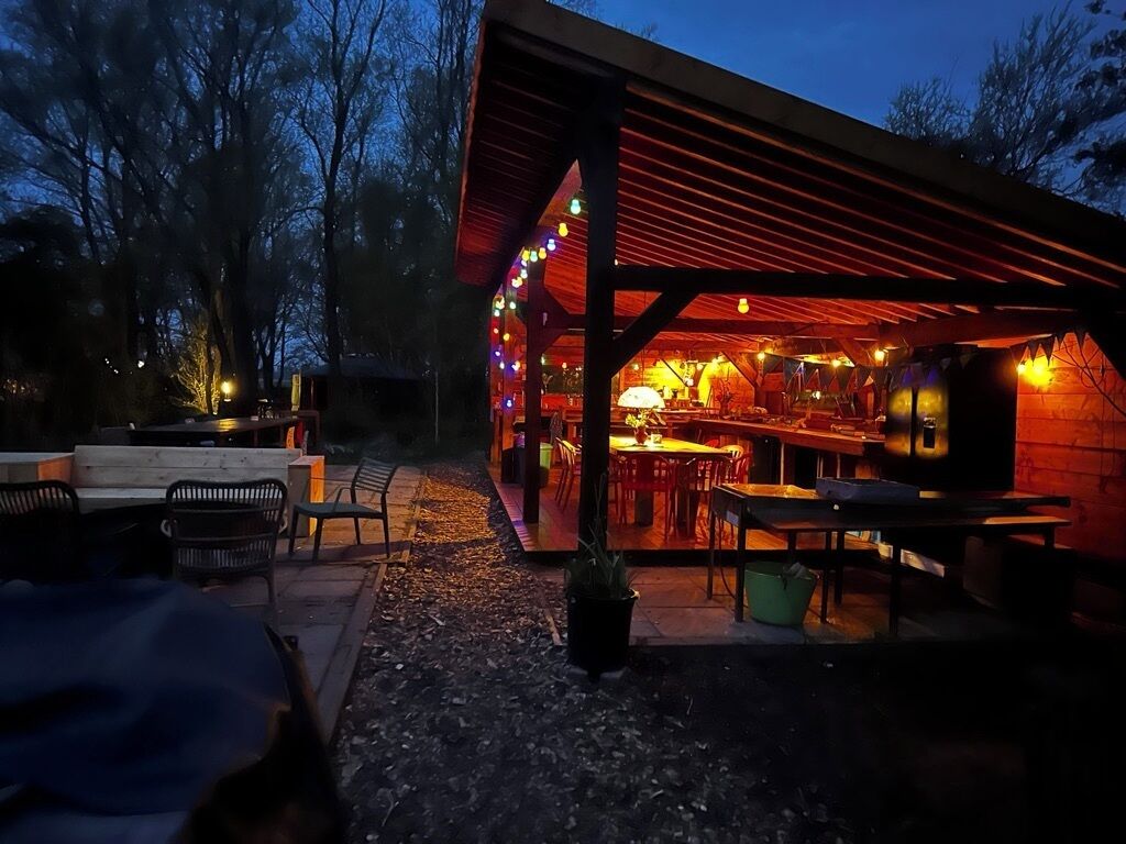 Ulkoterassi, jossa on pöytiä ja tuoleja, grilli ja valoketju.