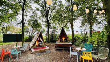 Un camping con una tienda de campaña, un hogar para fogata y asientos al aire libre.