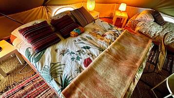Een tent met een bed, kussens, een lamp en een deken.