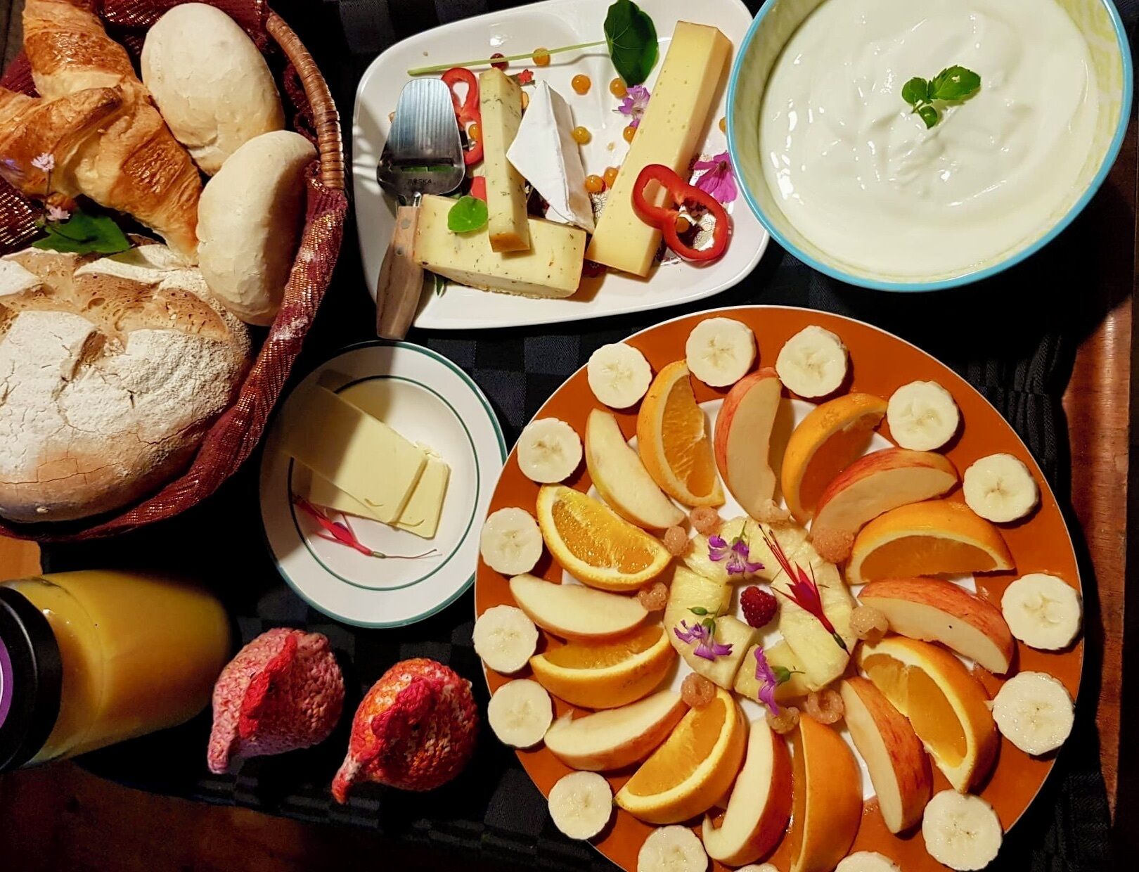 A variety of food items including bread, cheese, fruits, and a bowl of yogurt.