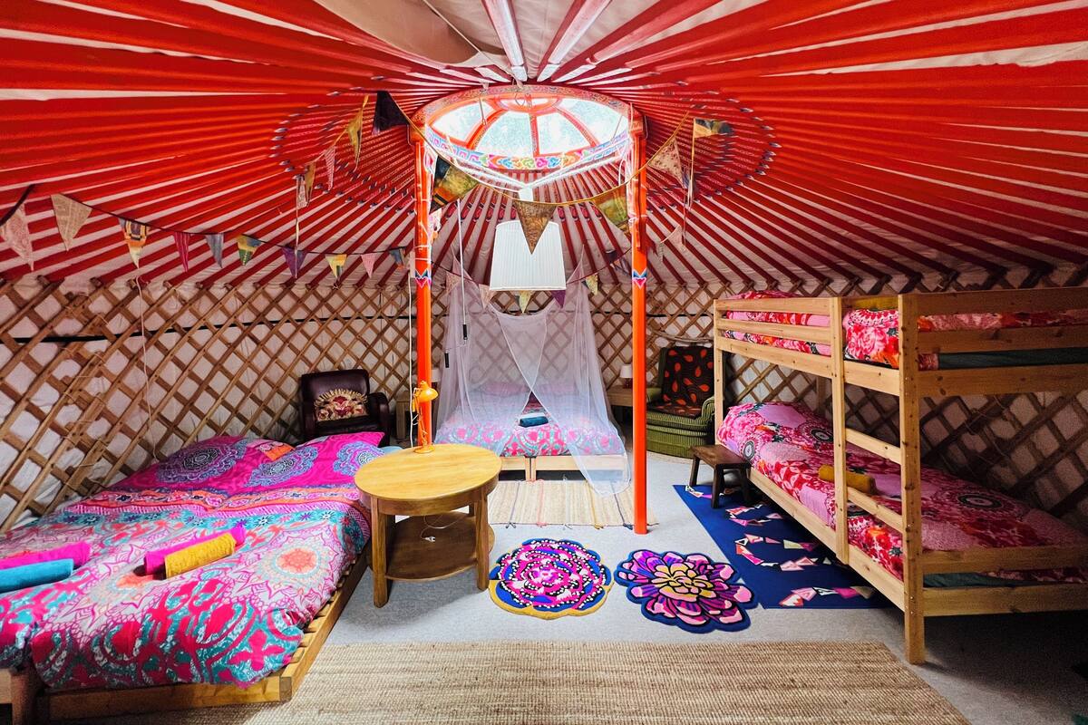 A cozy, well-decorated yurt with a central bed, a small table, and a bench.