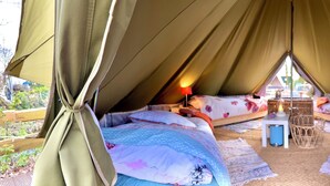Una carpa acogedora con dos camas, una mesita y una silla de mimbre.