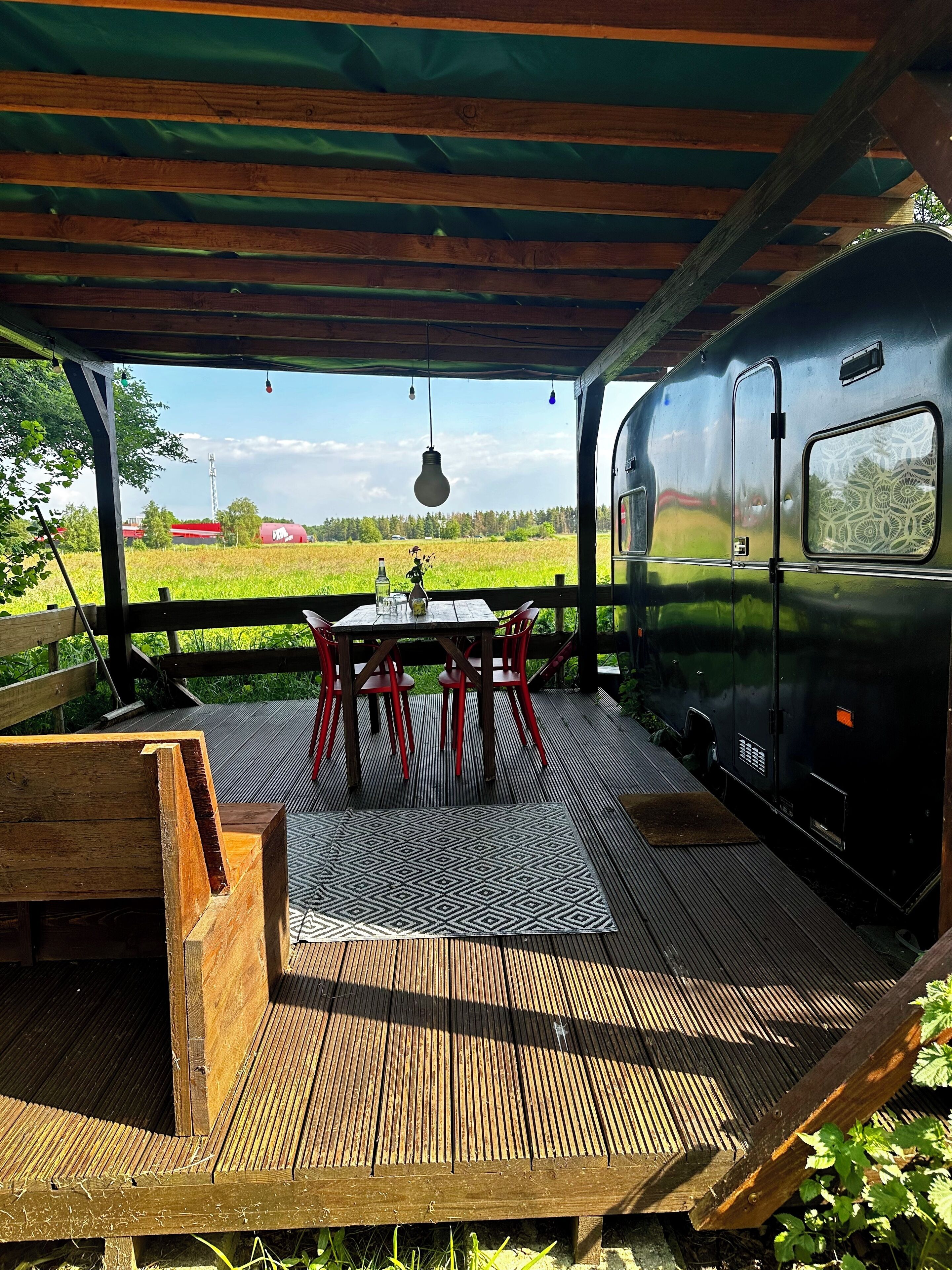 A covered outdoor seating area with a table and chairs, a wooden deck, and a view of a green field.