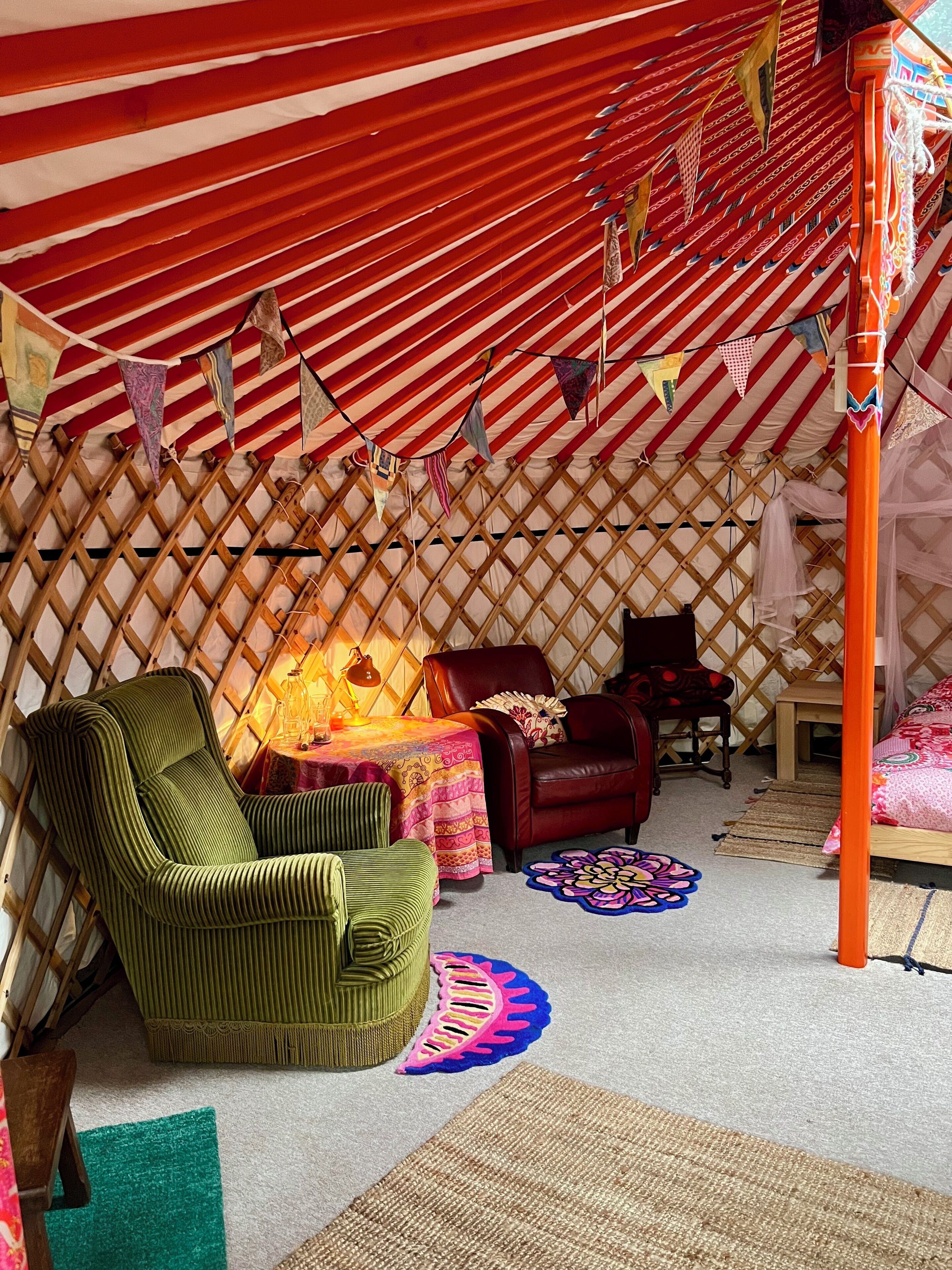 A cozy, striped tent interior with a green chair, a red sofa, and a small table with a lamp.