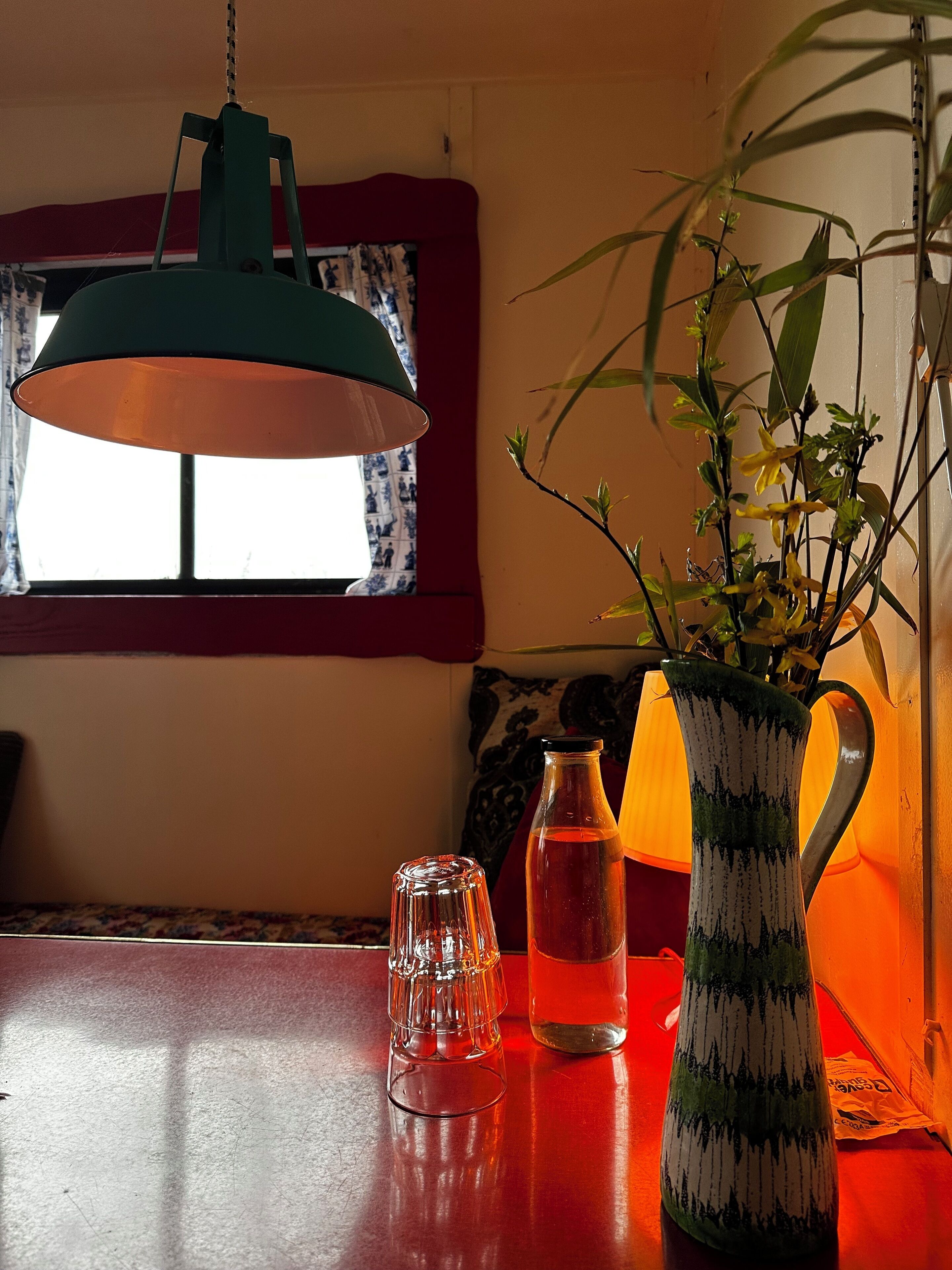 Een tafel met een groene lamp, een vaas met gele bloemen en een glazen fles.