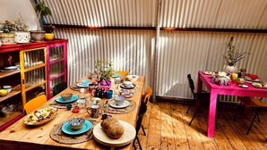 Un comedor con una mesa de madera dispuesta para una comida, rodeado de armarios coloridos y una pared de metal corrugado.