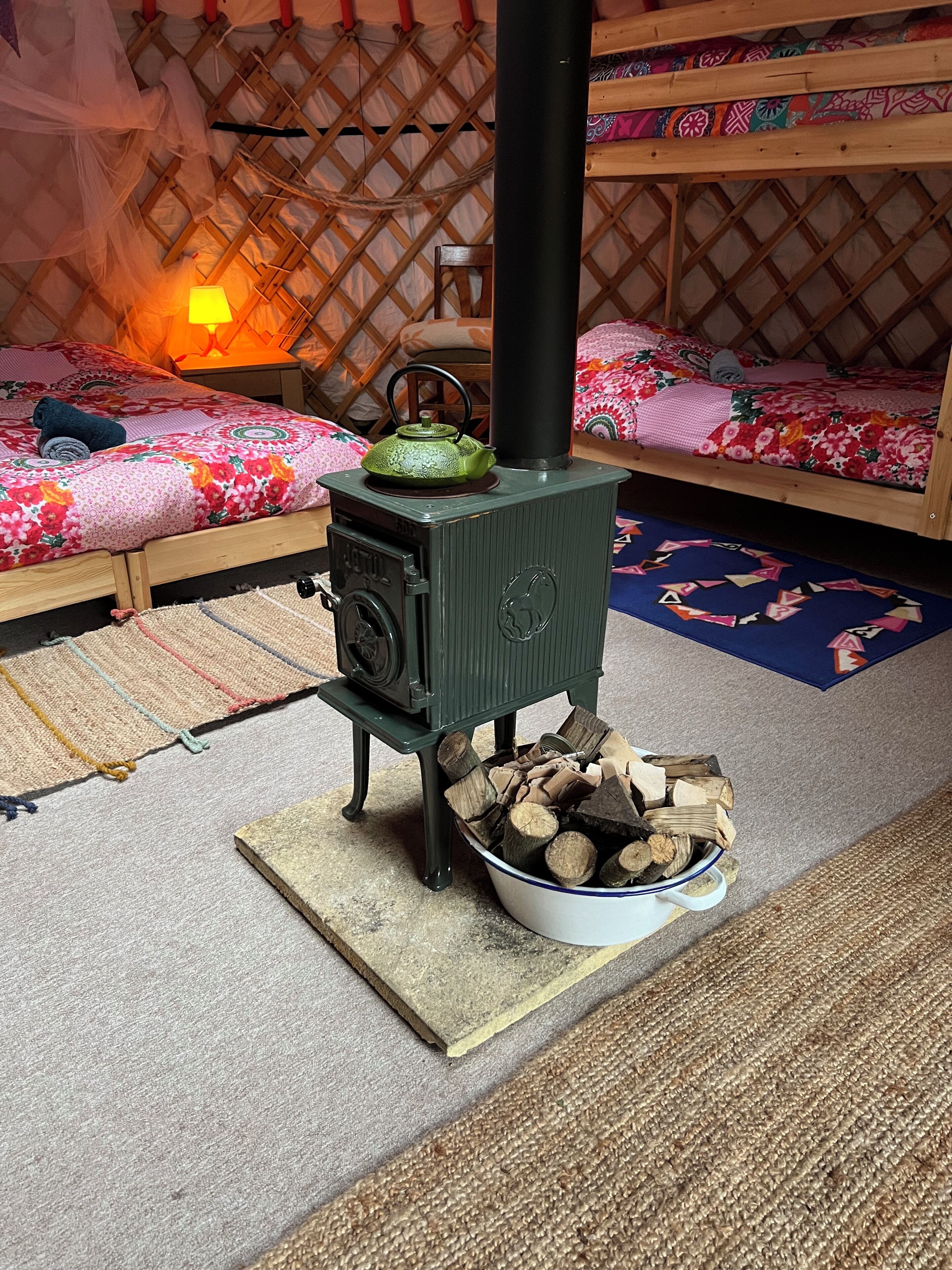 Una habitación acogedora con una estufa de leña, una cama con ropa de cama floral y una mesita con lámpara.