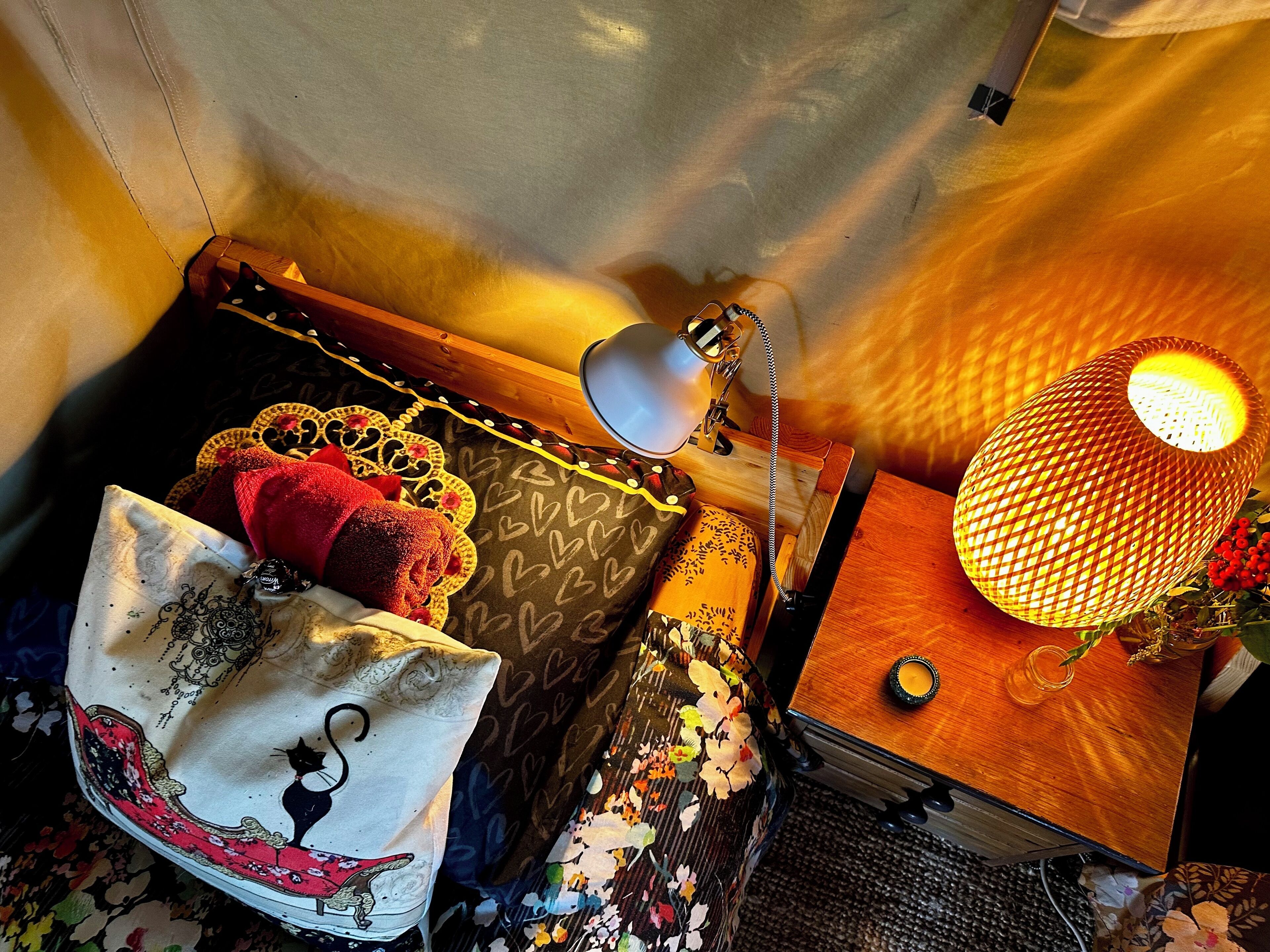 A cozy room with a bed, a bedside lamp, a decorative lamp, and a small table with a candle.