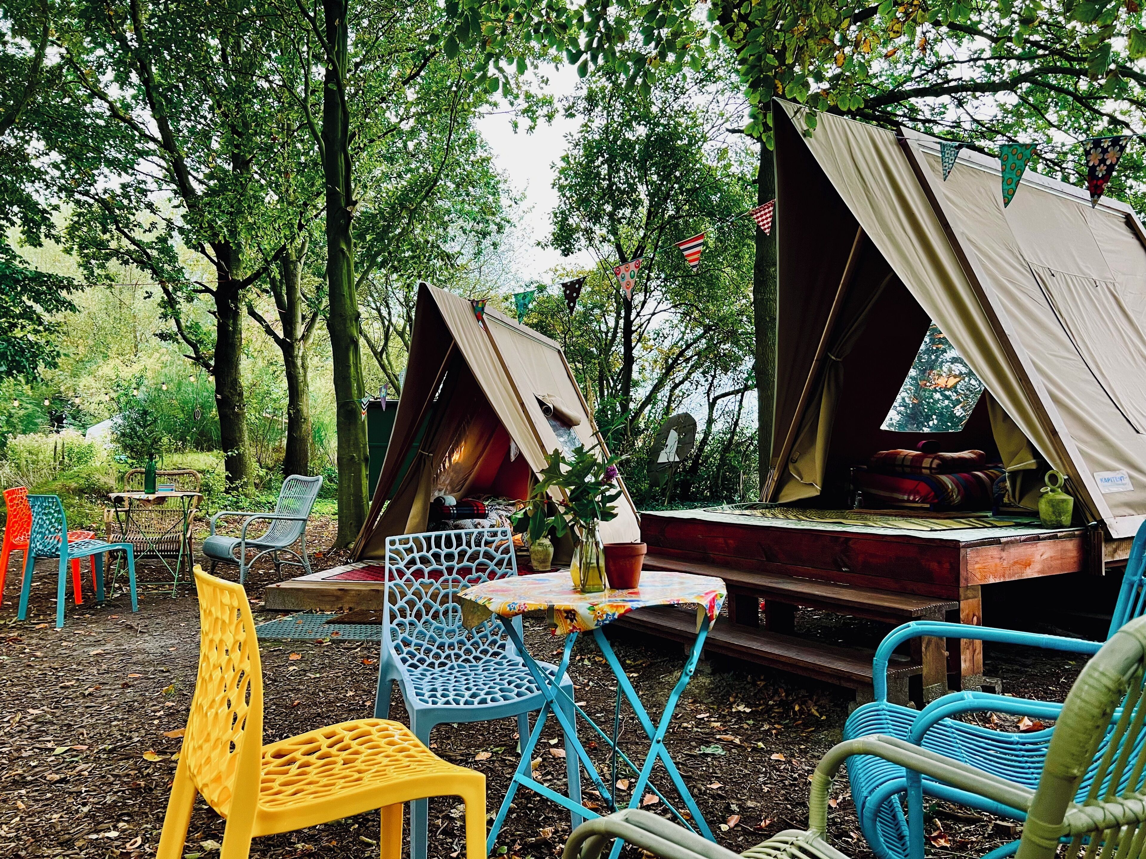 A campsite with two tents, a table, and colorful chairs.