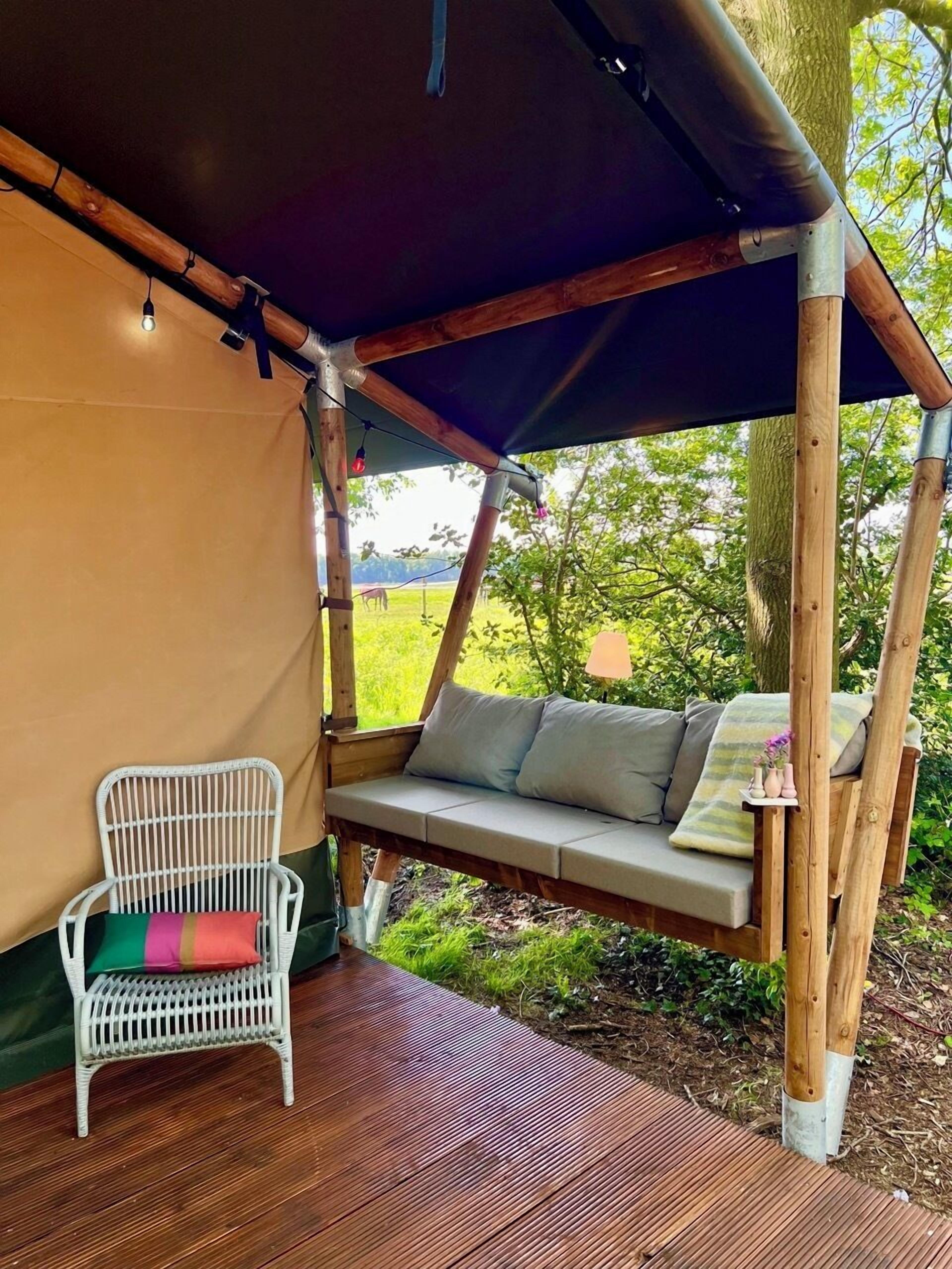 A wooden swing chair under a canopy, a white wicker chair, and a wooden deck.