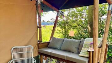 A wooden swing chair under a canopy, a white wicker chair, and a wooden deck.