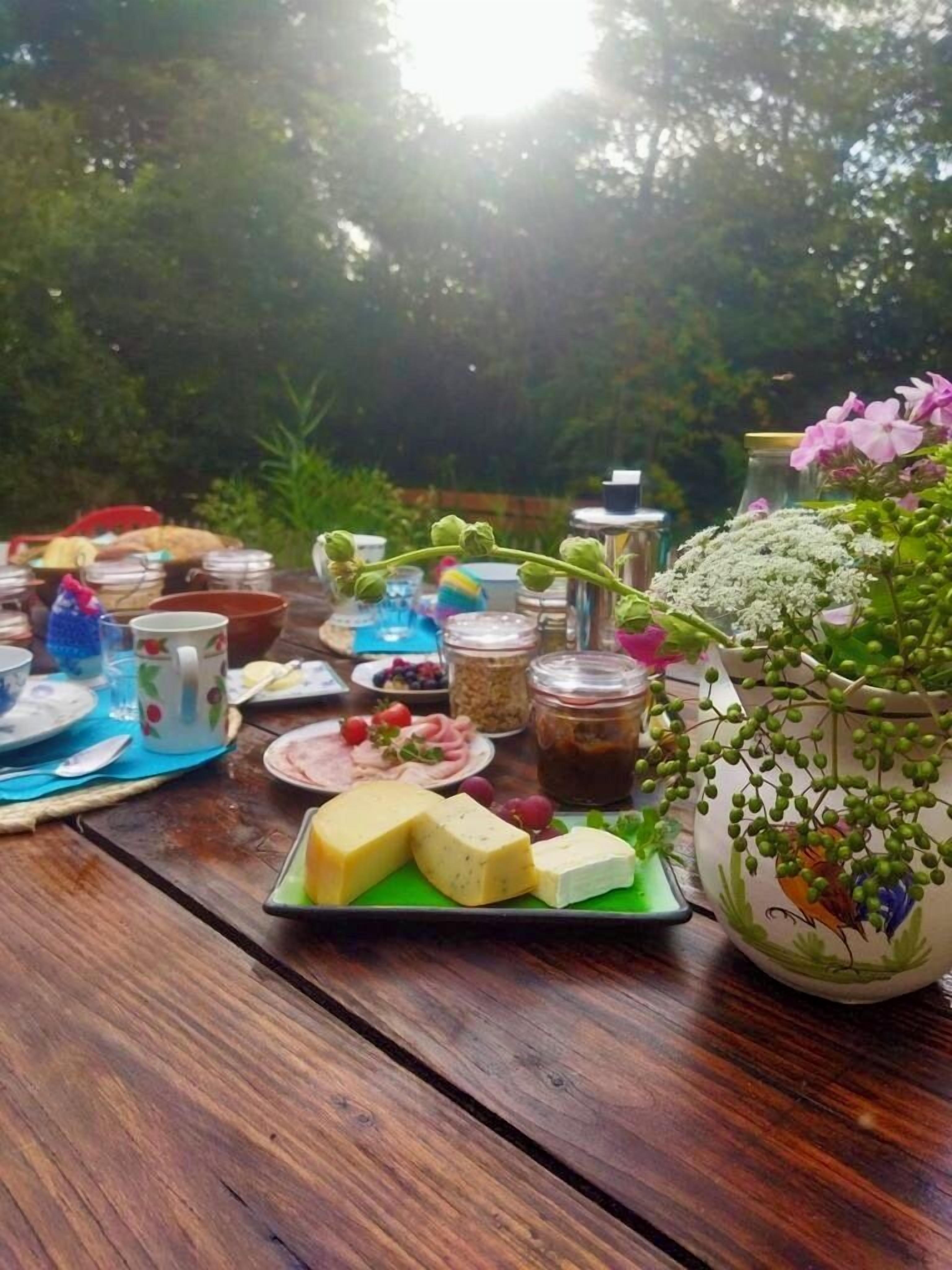 Une table en bois, sur laquelle sont disposés divers aliments et des bocaux, le tout entouré de verdure.