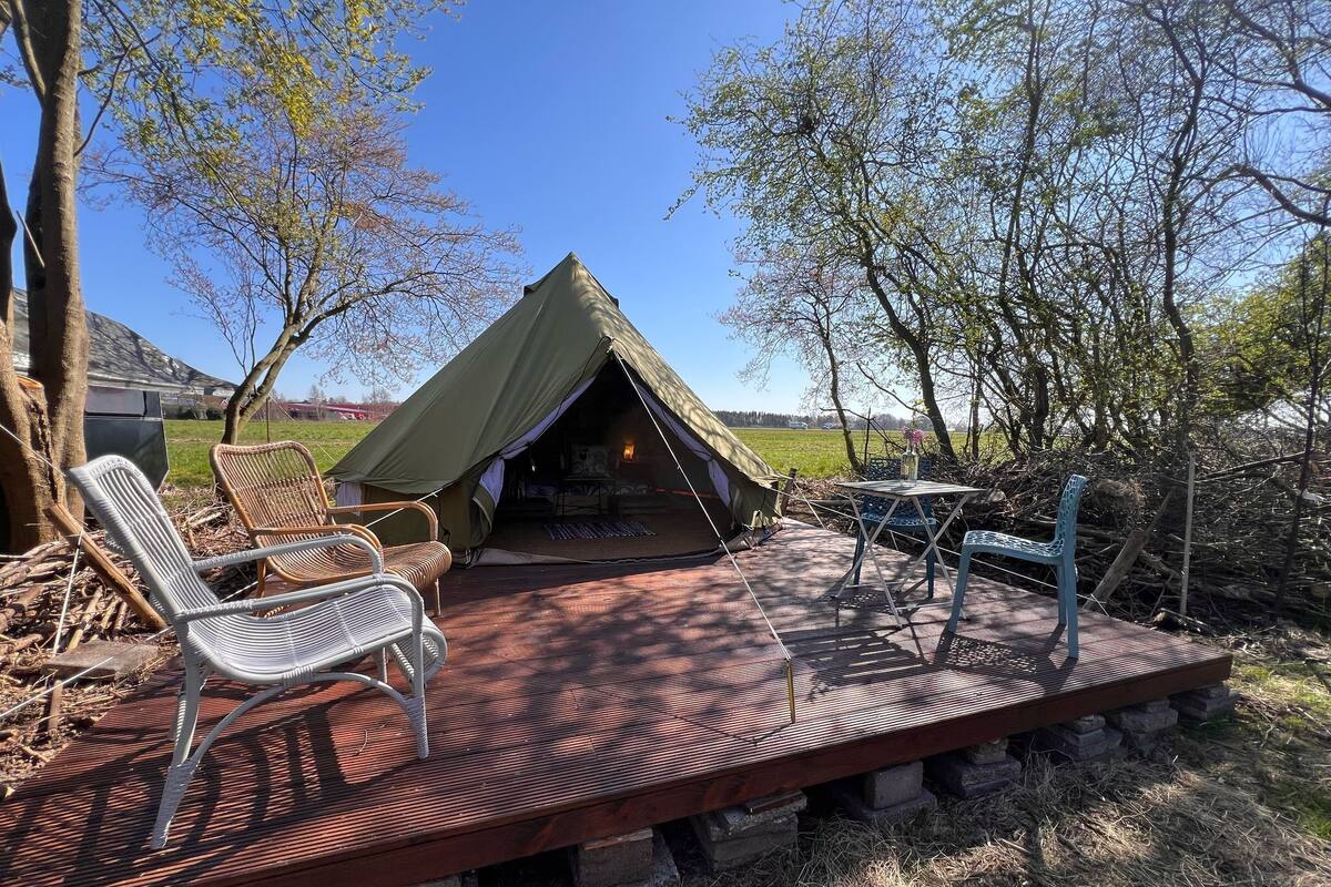 A tent with a wooden deck, wicker chairs, and a table.