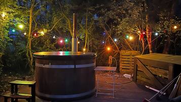 A wooden deck with a hot tub, string lights, and a wooden bench.