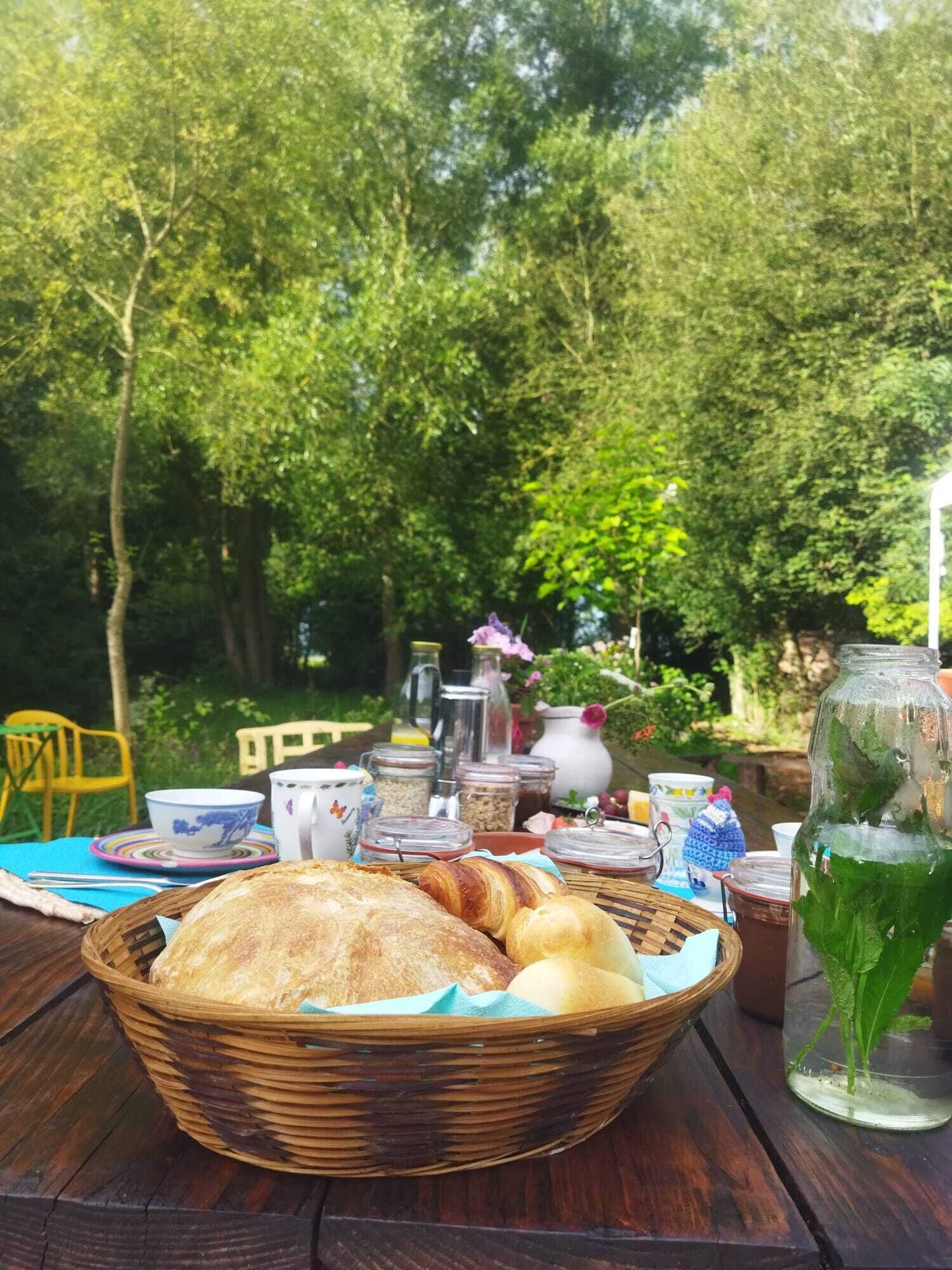 Een picknickopstelling met een mand vol brood, potten met sauzen en een glazen pot met muntblaadjes.
