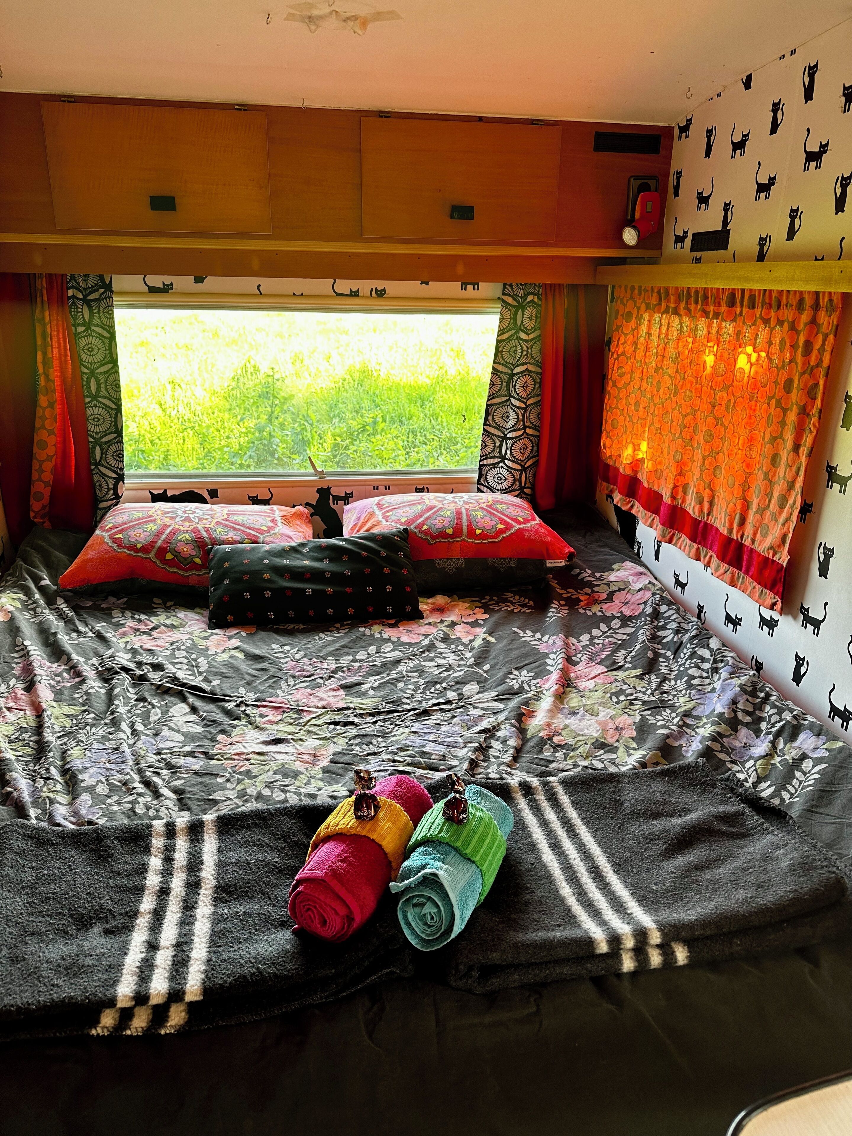 Een gezellige kamer met een bed, een raam met gordijnen en uitzicht op groen.