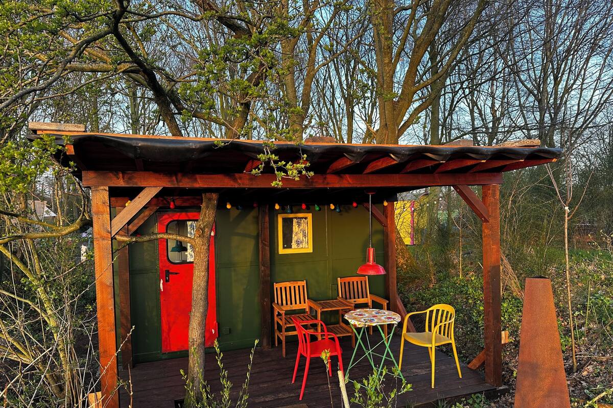 A rustic wooden structure with a red door, a small table with chairs, and a hanging light fixture.
