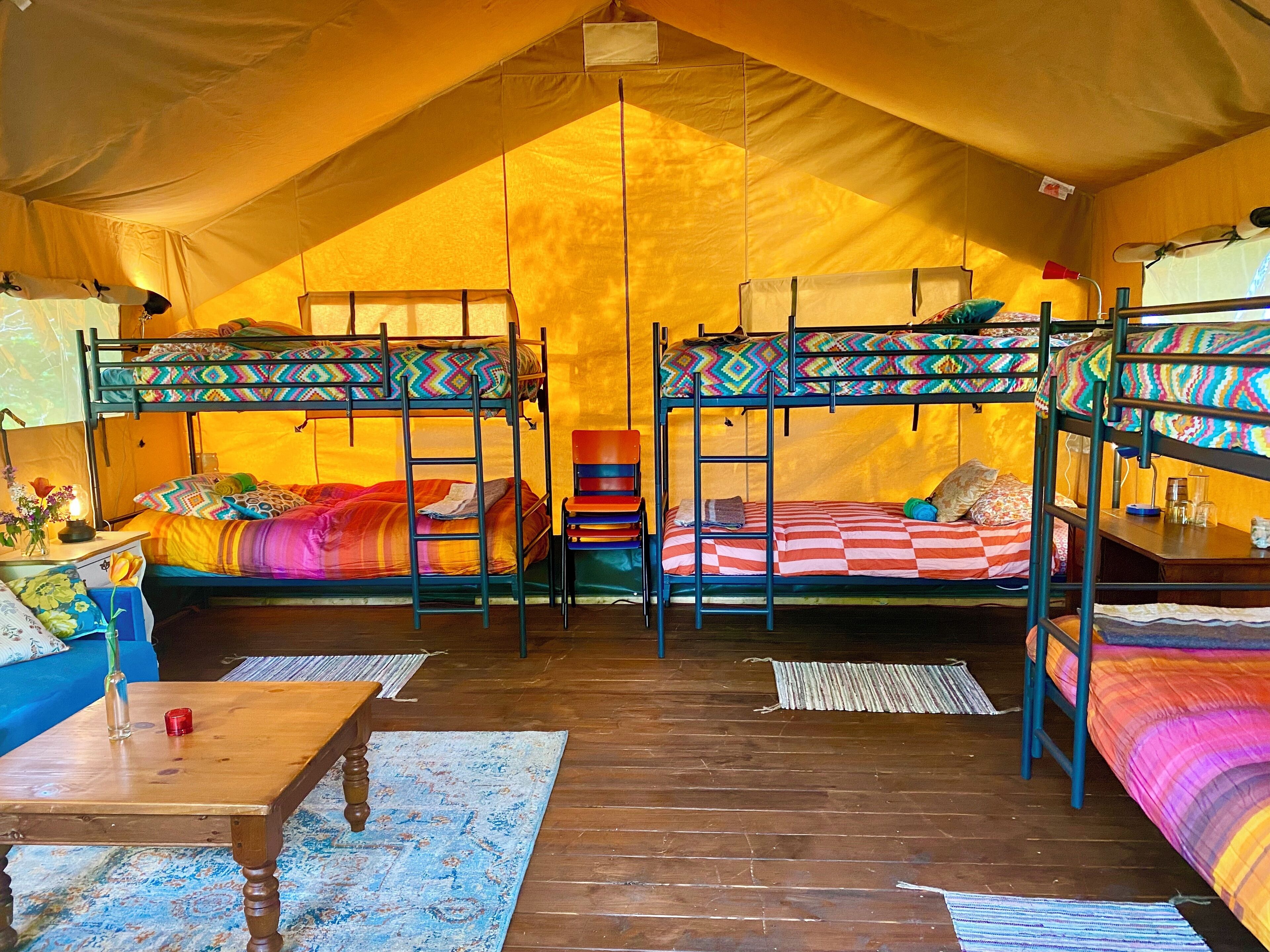 A tented accommodation with bunk beds, a wooden table, and a blue patterned rug.