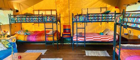 A tented accommodation with bunk beds, a wooden table, and a blue patterned rug.