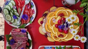 Una mesa con diversos alimentos, como pepinos en rodajas, tomates, naranjas y queso, sobre un mantel rojo.