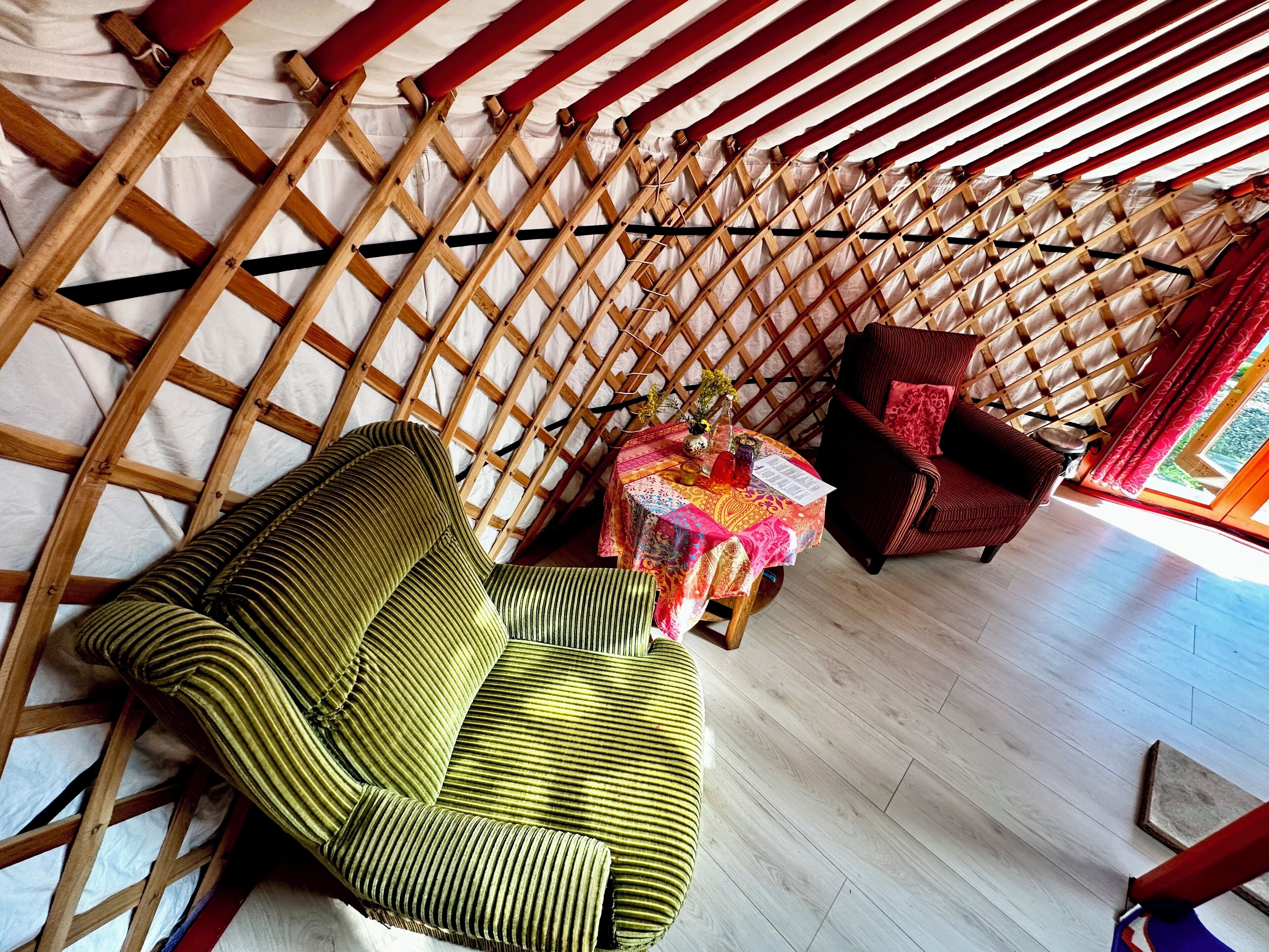 A room with a wooden lattice partition, a green striped sofa, a red armchair, and a small table with a colorful tablecloth.