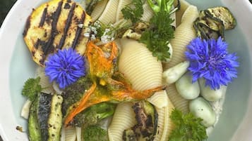 Un plato de comida con vegetales a la parrilla y pasta, adornado con perejil y flores azules.