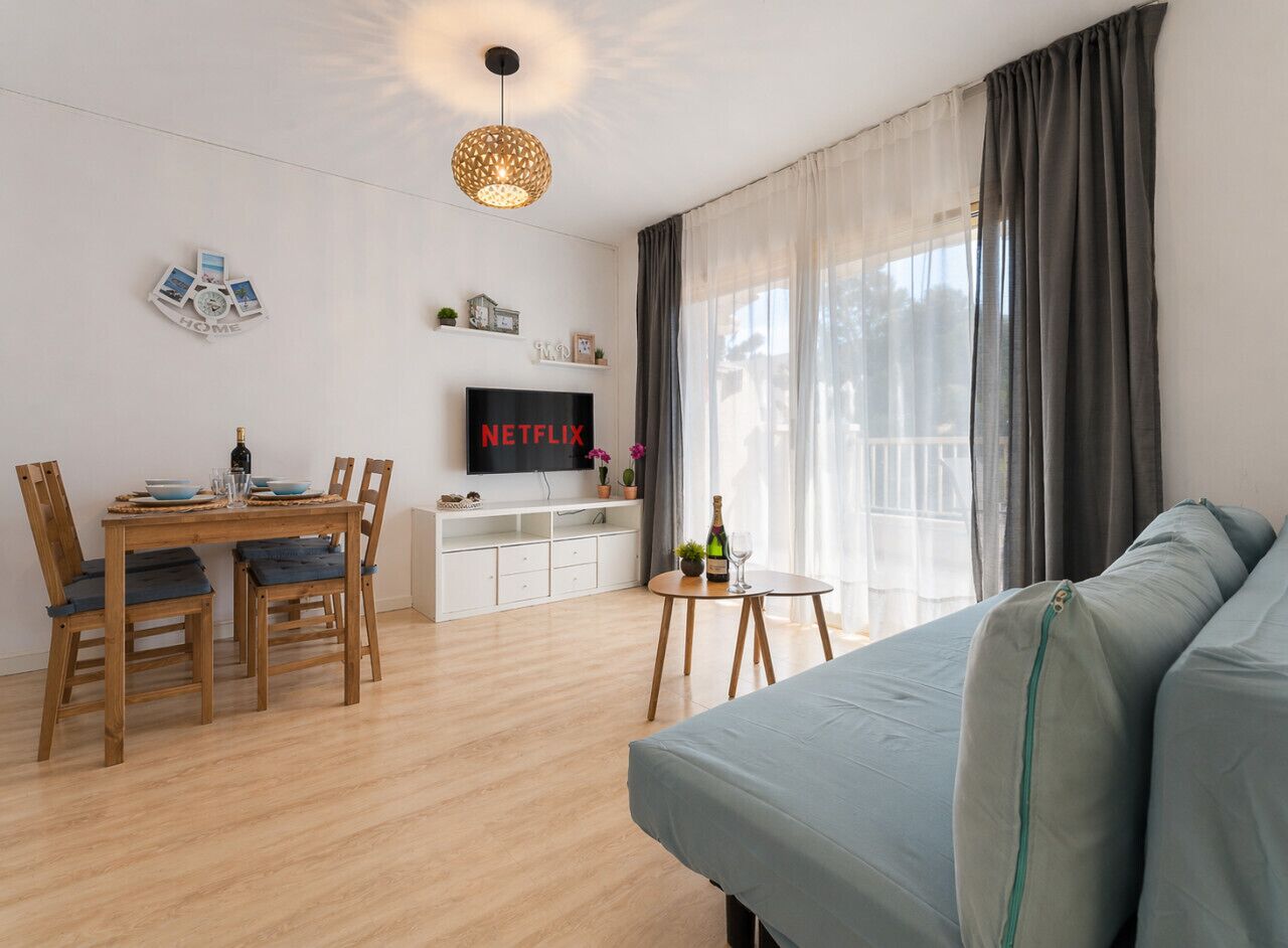 A modern living room with a wooden dining table, a sofa, a TV, and a balcony with curtains.