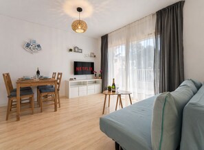 Een moderne woonkamer met een houten eettafel, een bank, een televisie en een balkon met gordijnen.