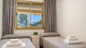 Un dormitorio con dos camas, una ventana con cortinas, una mesita de noche con una planta y toallas.