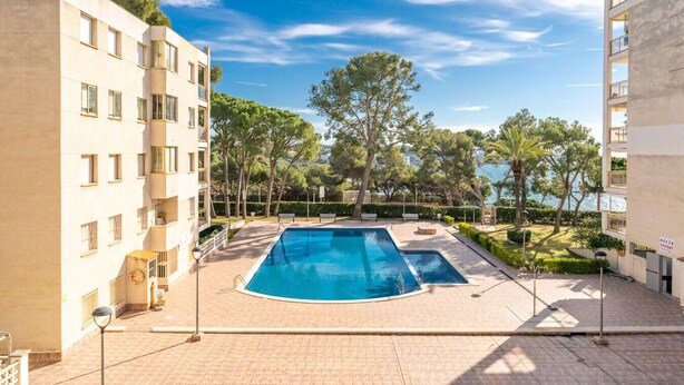 Una piscina rodeada de jardines con árboles y vistas al mar.