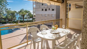 Un balcón con mesa lista para comer, sillas y vistas a una piscina y edificios.
