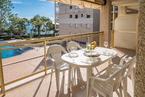A balcony with a table set for dining, chairs, and a view of a swimming pool and buildings.