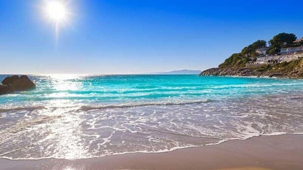A beach with clear turquoise water, a sandy shore, and a building on a cliff in the background. - Salou | Modern | Cozy (5pax) Wifi | AA|Parking (Salou)