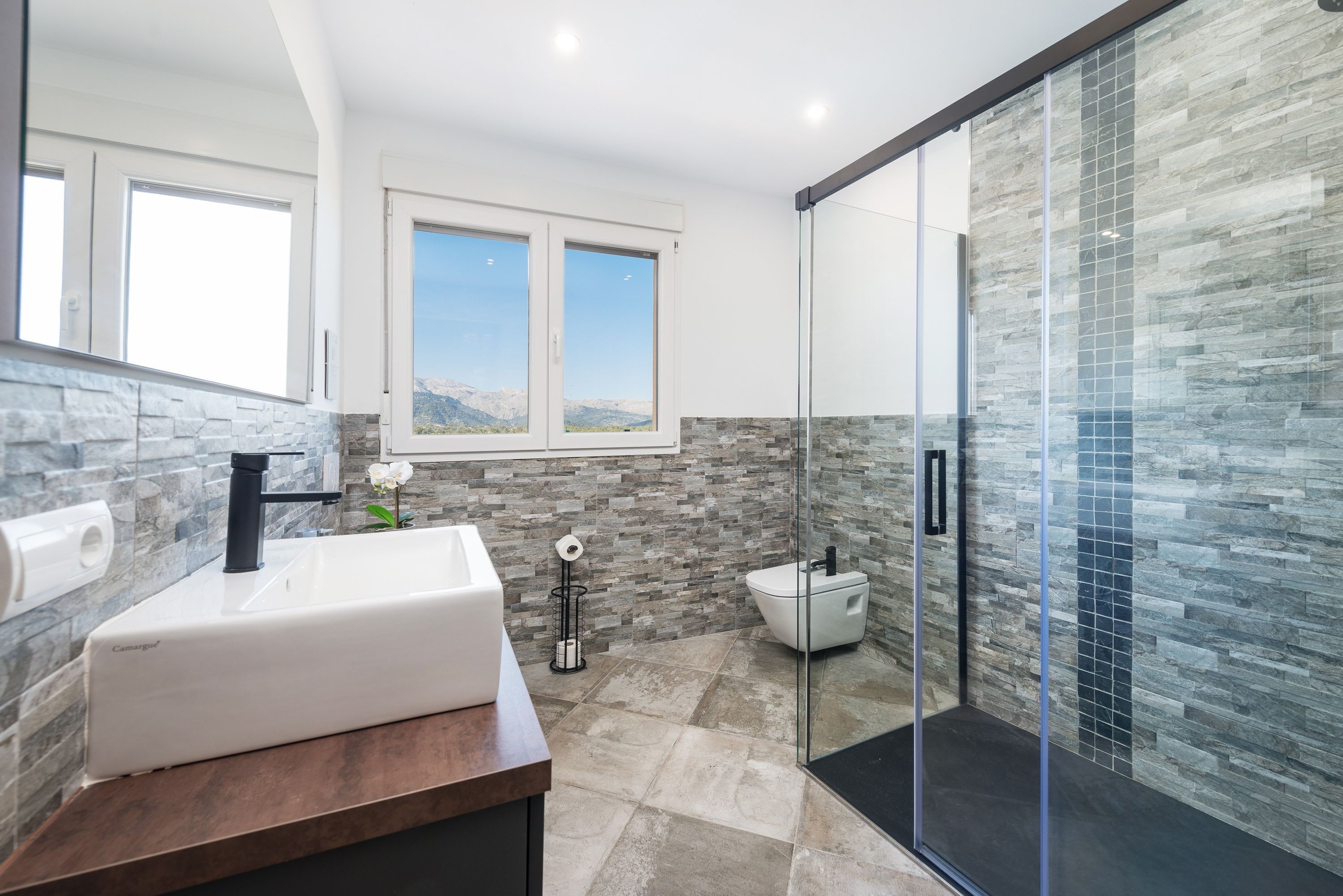A modern bathroom with a stone backsplash, a white sink, and a glass shower enclosure.