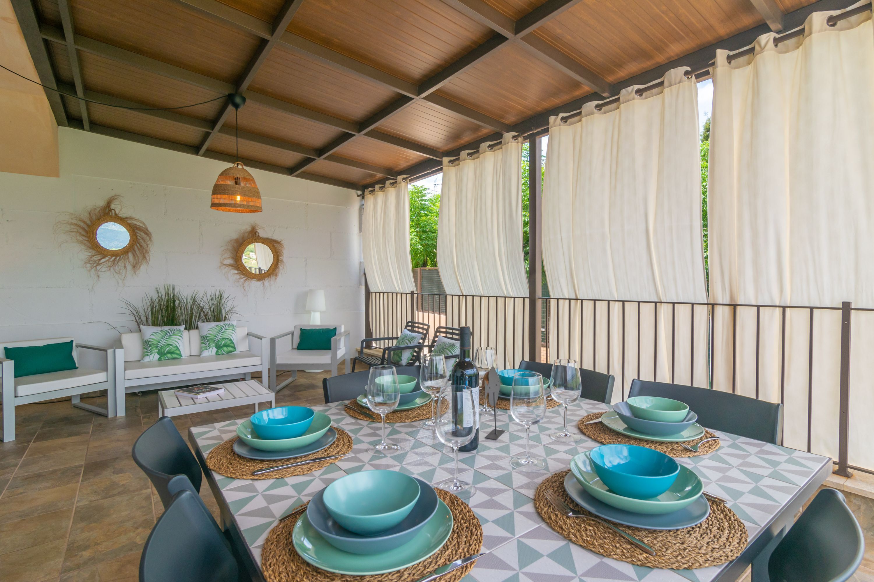 A dining area with a table set for six, surrounded by chairs, with a view of greenery outside.