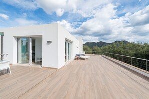 Un edificio moderno con una terrazza in legno, porte scorrevoli in vetro e vista sulle montagne.
