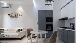 A modern living room with a sofa, a round table, and chairs. There is a kitchen area with cabinets and a stove. - Tashkent city Bulevard Fontaine (Tashkent)