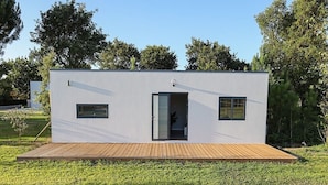 Een modern, gelijkvloers gebouw met een plat dak, een houten terras en een kleine deur.