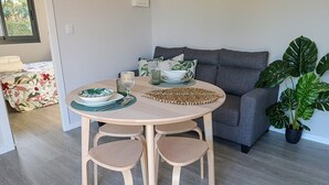 Een ronde houten tafel met vier stoelen, een grijze bank en een potplant in een woonkamer.