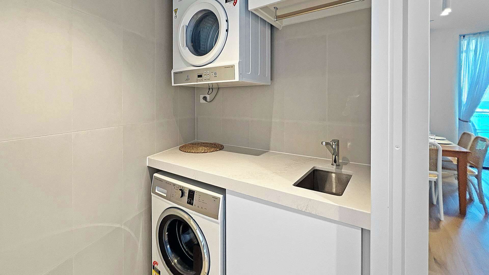 A compact kitchen with a washing machine, a sink, and a dining area visible through an open door.