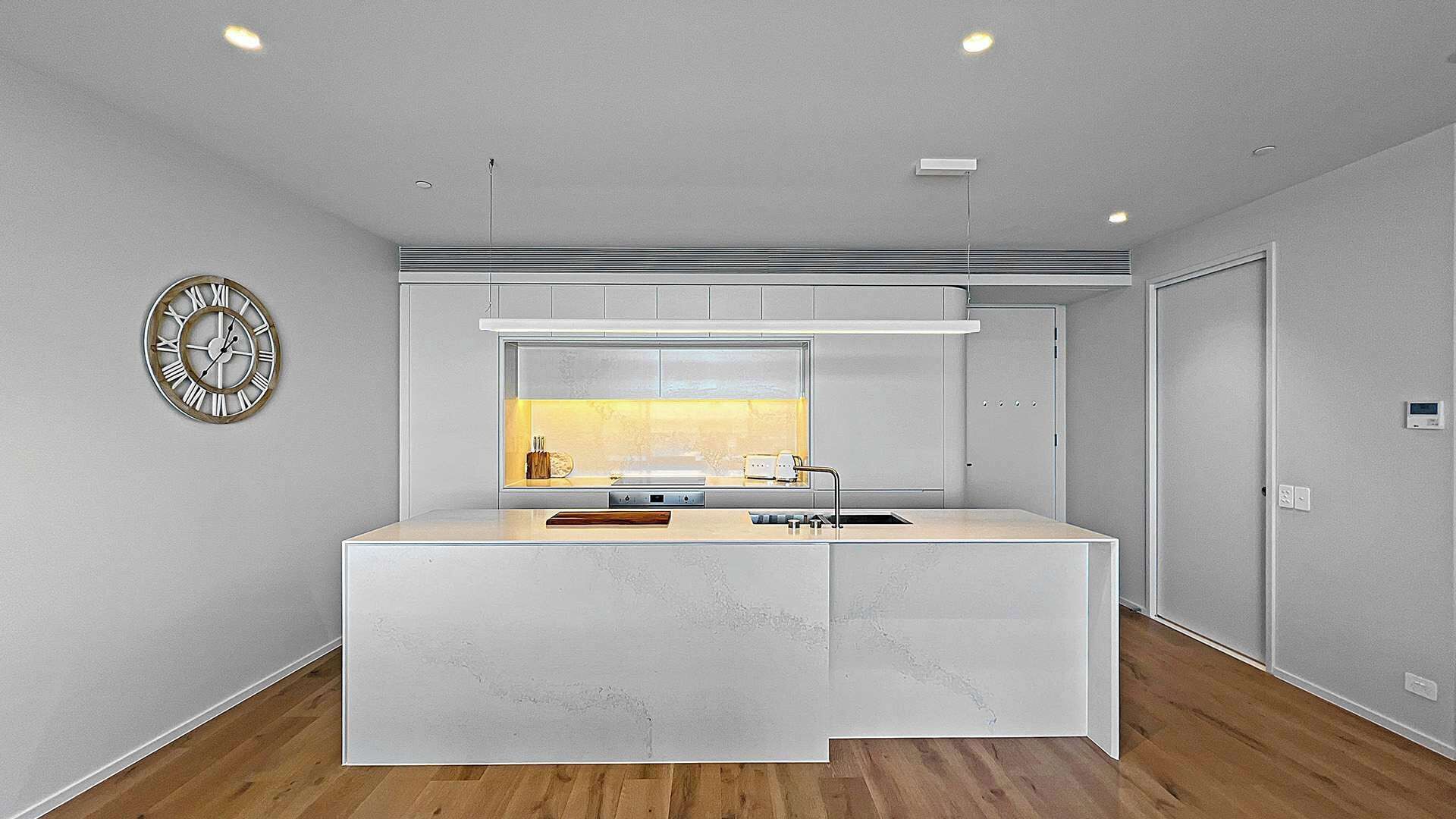 A modern kitchen with a central island, built-in appliances, and a clock on the wall.