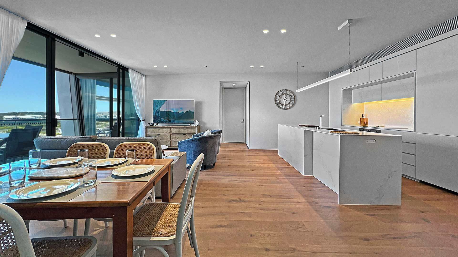 A modern kitchen with a central island, a dining area with a view, and a large window overlooking a landscape.