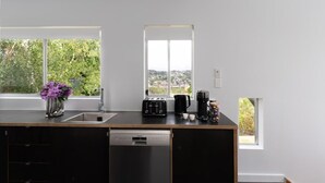 A modern kitchen with a dishwasher, a toaster, and a coffee maker on the counter, and a window with a view of greenery outside.