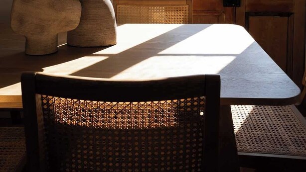 A dining area with a table and chairs, a wooden door with a view of greenery, and a textured sculpture on the table.