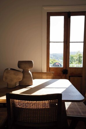 A dining area with a table and chairs, a wooden door with a view of greenery, and a textured sculpture on the table. - Launceston Cottage Charming 3 bedroom home (Launceston)