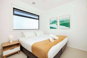 A bedroom with a bed, a nightstand, a window, and two wall-mounted paintings. - Northside Townhouse, Geelong (Norlane)