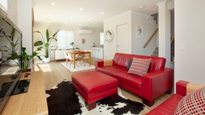 En moderne stue med en rød sofa, en måtte af sort-hvid kvæder og et spiseområde med et træbord og stole.