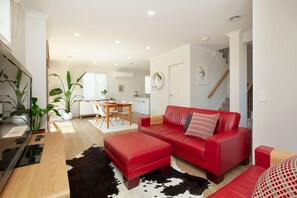 Ein modernes Wohnzimmer mit einem roten Sofa, einem schwarz-weißen Kuhfellteppich und einem Essbereich mit einem Holztisch und Stühlen.