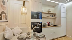 A modern kitchen with white cabinets, a Bosch microwave, and a sink. There is a dining area with a round table set for four, and a sofa with cushions.
