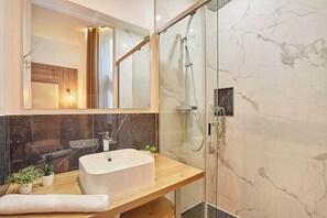A modern bathroom with a freestanding bathtub, a glass-enclosed shower, and marble walls.